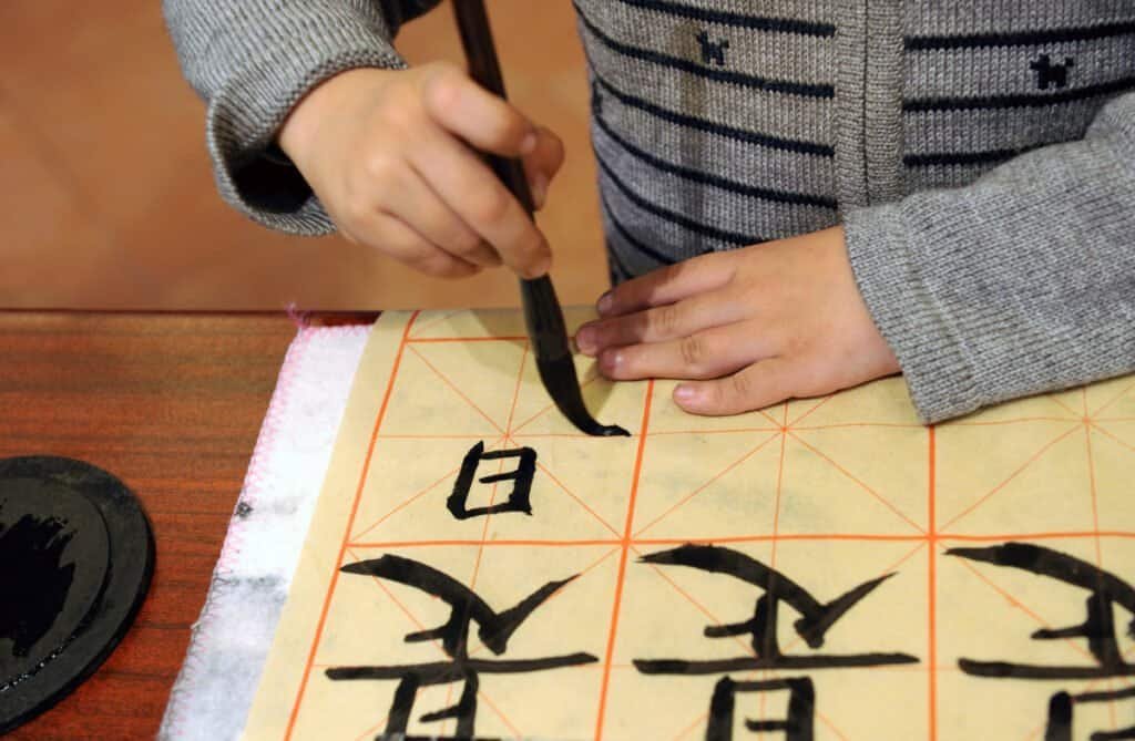 A close-up of a hand repeatedly writing the same Chinese character, illustrating the power of consistent, boring practice.
